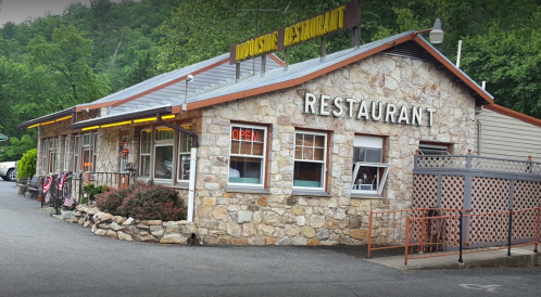 A stone building with a sign reading "Restaurant" and an "Open" neon sign, surrounded by greenery.