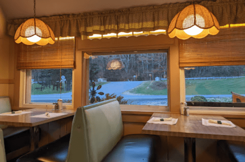 Cozy diner interior with green booths, wooden tables, and warm lighting, overlooking a quiet road outside.