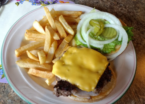 A plate with a cheeseburger topped with lettuce, pickles, and onions, served with a side of golden French fries.