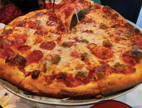 A large pizza topped with pepperoni, sausage, and melted cheese, served on a metal tray.