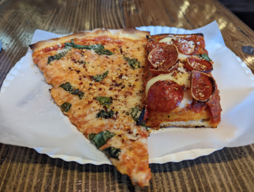 A slice of cheese and basil pizza next to a square pepperoni pizza on a paper plate.