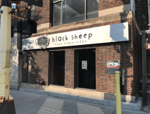 Exterior of "Black Sheep Coal Fired Pizza" restaurant, featuring a brick facade and a sign above the entrance.