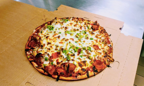 A freshly baked pizza with melted cheese, pepperoni, and green peppers on a cardboard pizza box.