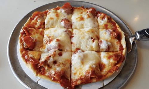 A freshly baked pizza with pepperoni and melted cheese, cut into square slices on a metal tray.