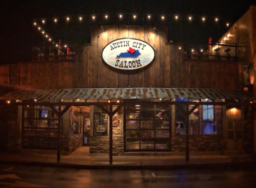Exterior of Austin City Saloon at night, featuring wooden architecture and string lights illuminating the entrance.