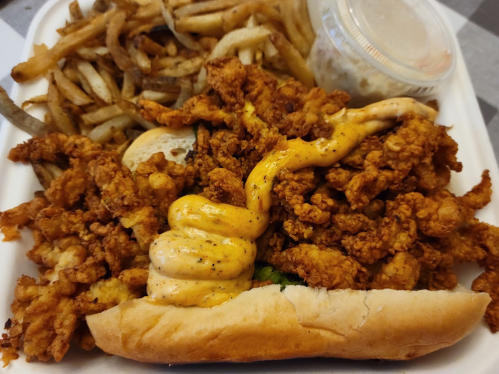 A plate of crispy fried chicken, topped with sauce, served with a side of fries and a small container of coleslaw.