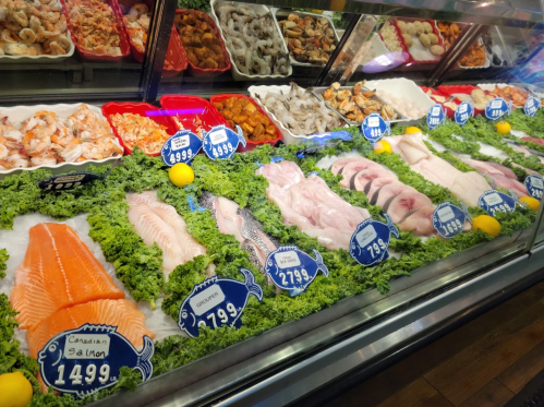 A seafood display featuring various fish and shellfish on ice, with price tags and garnished with lettuce and lemons.