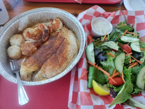 A plate of seasoned fish fillet with potatoes and a side salad of mixed greens, tomatoes, and cucumber.