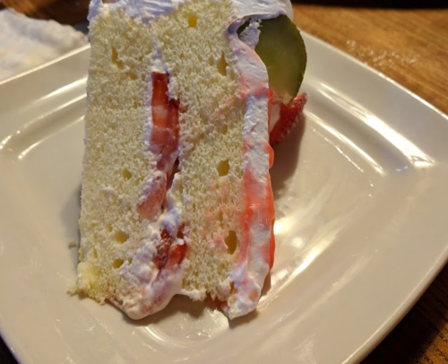 A slice of white cake with whipped cream and strawberries on a plate.