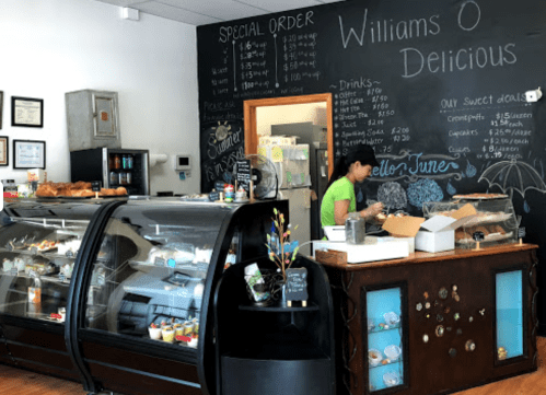 A cozy café interior with a display case, chalkboard menu, and a staff member preparing orders.