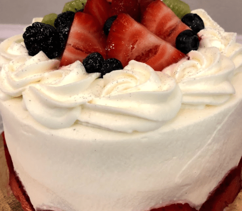 A round cake topped with whipped cream and an assortment of fresh berries and sliced strawberries.