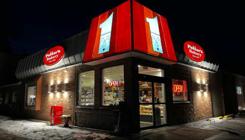 A brightly lit bakery at night, featuring a large "1" sign and an "OPEN" sign, with snow on the ground.