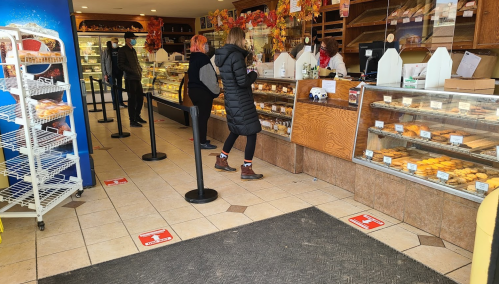 A bakery interior with customers in line, displaying pastries and baked goods behind a glass counter.