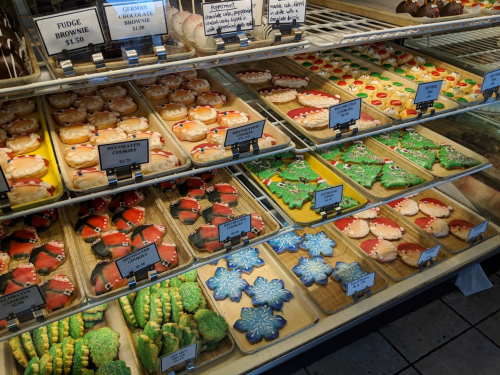 A display of colorful holiday cookies and brownies in a bakery, featuring festive shapes and decorations.