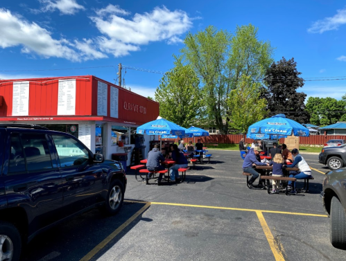 A vibrant outdoor eatery with blue umbrellas, picnic tables, and customers enjoying food on a sunny day.