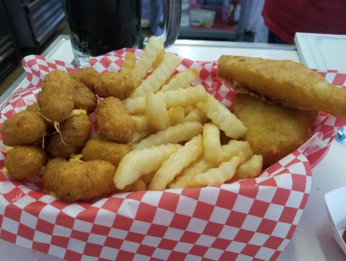 A basket with golden fried snacks: cheese curds, crinkle-cut fries, and a fried sandwich, all on a red-checkered liner.