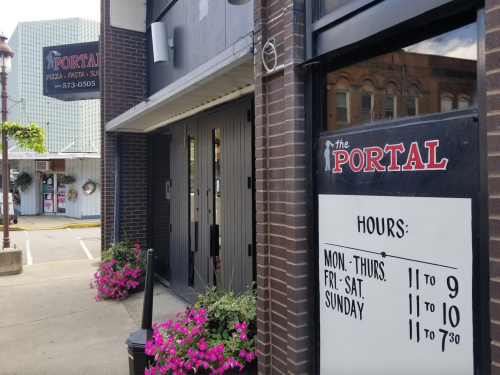 Exterior view of The Portal restaurant, featuring a sign with hours and colorful flowers in front.