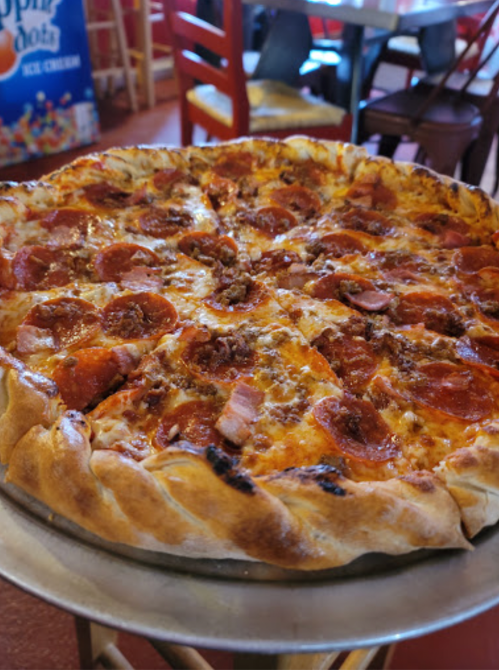 A close-up of a pepperoni pizza with a thick crust, served on a metal tray in a casual dining setting.