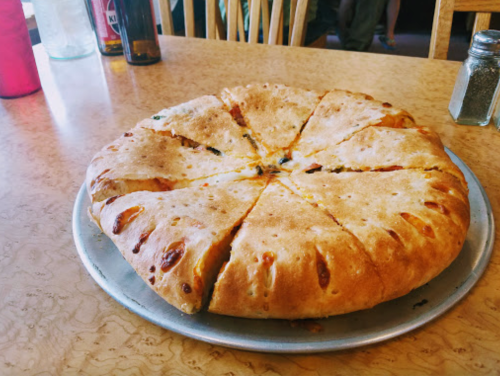 A round, golden-brown calzone cut into wedges, resting on a silver pizza tray on a wooden table.