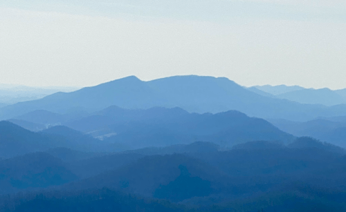 A serene landscape of layered blue mountains under a light sky, creating a tranquil and misty atmosphere.