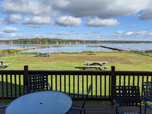 Scenic view of a lake with picnic tables and a dock, under a partly cloudy sky.