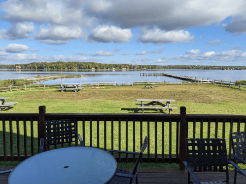 Scenic view of a lake with picnic tables and a dock, under a partly cloudy sky.