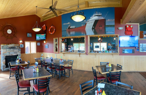 Cozy restaurant interior with wooden decor, tables, and a large mural of a ship on the wall.