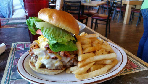 A juicy burger with lettuce, tomato, cheese, and bacon, served with a side of crispy French fries on a plate.