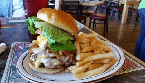 A juicy burger with lettuce, tomato, cheese, and bacon, served with a side of crispy French fries on a plate.