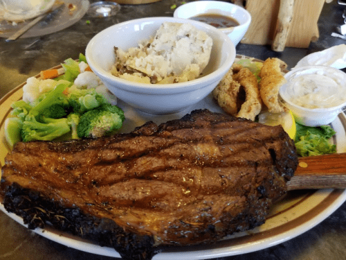 A plate featuring a large grilled steak, mashed potatoes, broccoli, and crispy onion rings.