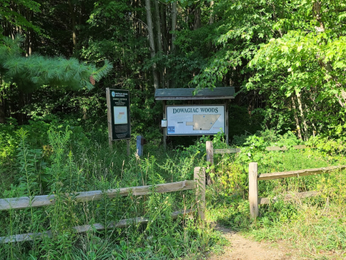 Signage at the entrance of Dowagiac Woods, surrounded by lush greenery and a wooden fence.
