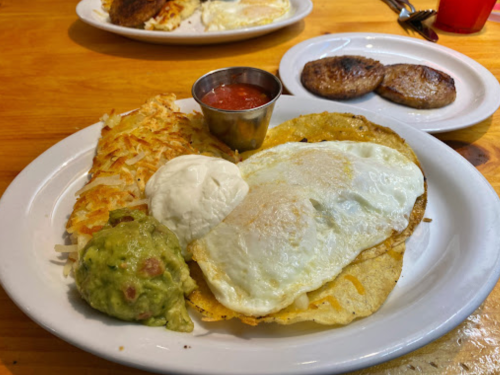 A plate of breakfast featuring eggs, guacamole, hash browns, salsa, and two sausage patties.