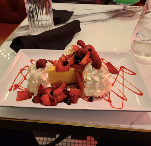 A dessert plate featuring cheesecake topped with strawberries, raspberries, and whipped cream, drizzled with sauce.