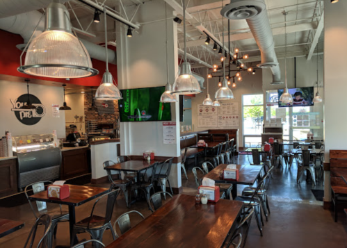 Bright, modern restaurant interior with metal tables, pendant lights, and a large TV on the wall.