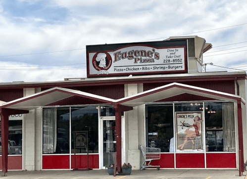 Exterior of Eugene's Pizza restaurant with a sign displaying menu items like pizza, chicken, and burgers.
