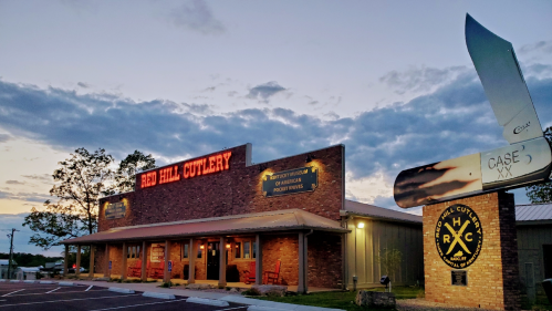 Exterior of Red Hill Cutlery at dusk, featuring a large knife sign and a brick building with illuminated signage.