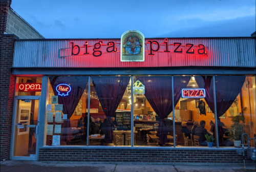 A cozy pizza restaurant with a glowing "open" sign and warm interior, featuring red curtains and a welcoming atmosphere.