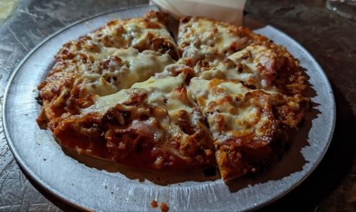 A freshly baked pizza with melted cheese and toppings, served on a round metal tray with one slice removed.