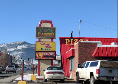 A roadside view featuring a casino sign and a pizza restaurant, with mountains in the background and clear blue skies.