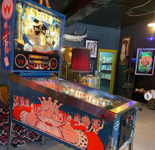 A colorful pinball machine featuring a king design, set in a vibrant arcade with various decor in the background.