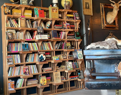 A wooden bookshelf filled with various books, magazines, and decorative items, set against a dark wall.