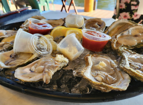 A platter of fresh oysters on ice, accompanied by lemon wedges and dipping sauces.