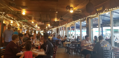 A bustling restaurant interior with diners at tables, string lights, and a lively atmosphere.