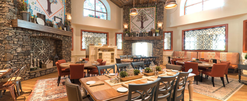 Cozy restaurant interior with stone walls, wooden tables, and decorative windows, featuring a warm, inviting atmosphere.