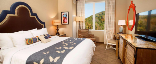 Cozy hotel room with a large bed, decorative accents, a TV, and a view of nature through a window.