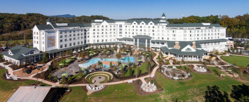 Aerial view of a large hotel with a pool and landscaped gardens, surrounded by trees and mountains in the background.