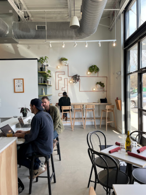 A modern café interior with plants on the wall, patrons working on laptops, and a bright, open atmosphere.