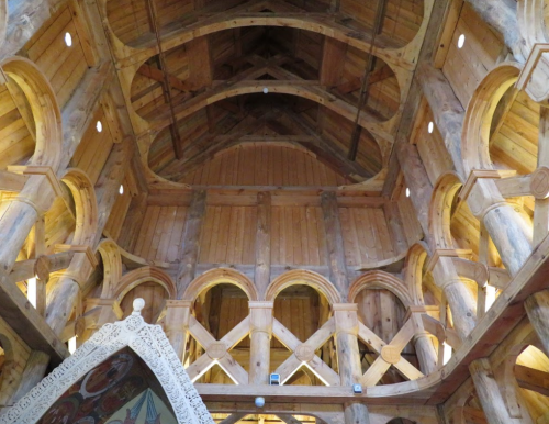 Interior view of a wooden structure with high arches, intricate carvings, and warm lighting.