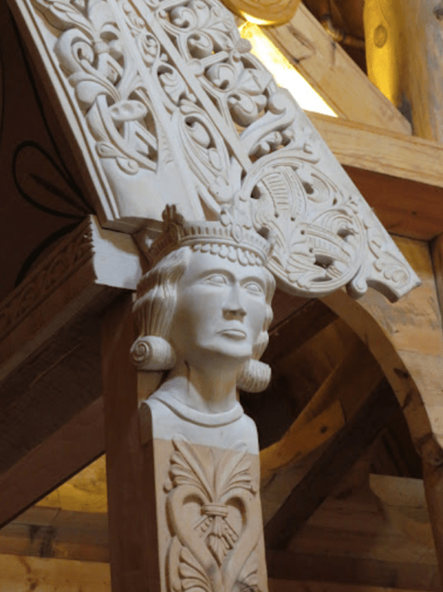 Carved wooden figure of a woman with intricate floral designs above, set in a rustic wooden structure.
