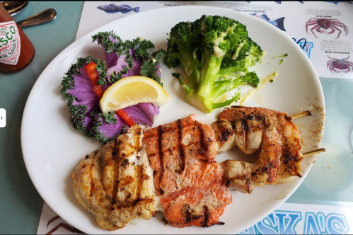 Grilled seafood platter with shrimp and fish, served with broccoli, salad, and lemon on a white plate.